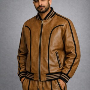 Pu&ograve; includere: Giacca bomber e pantaloni coordinati in pelle marrone con strisce e finiture nere. La giacca ha una chiusura con zip frontale e colletto e polsini a coste. I pantaloni hanno una vita con coulisse e tasche.