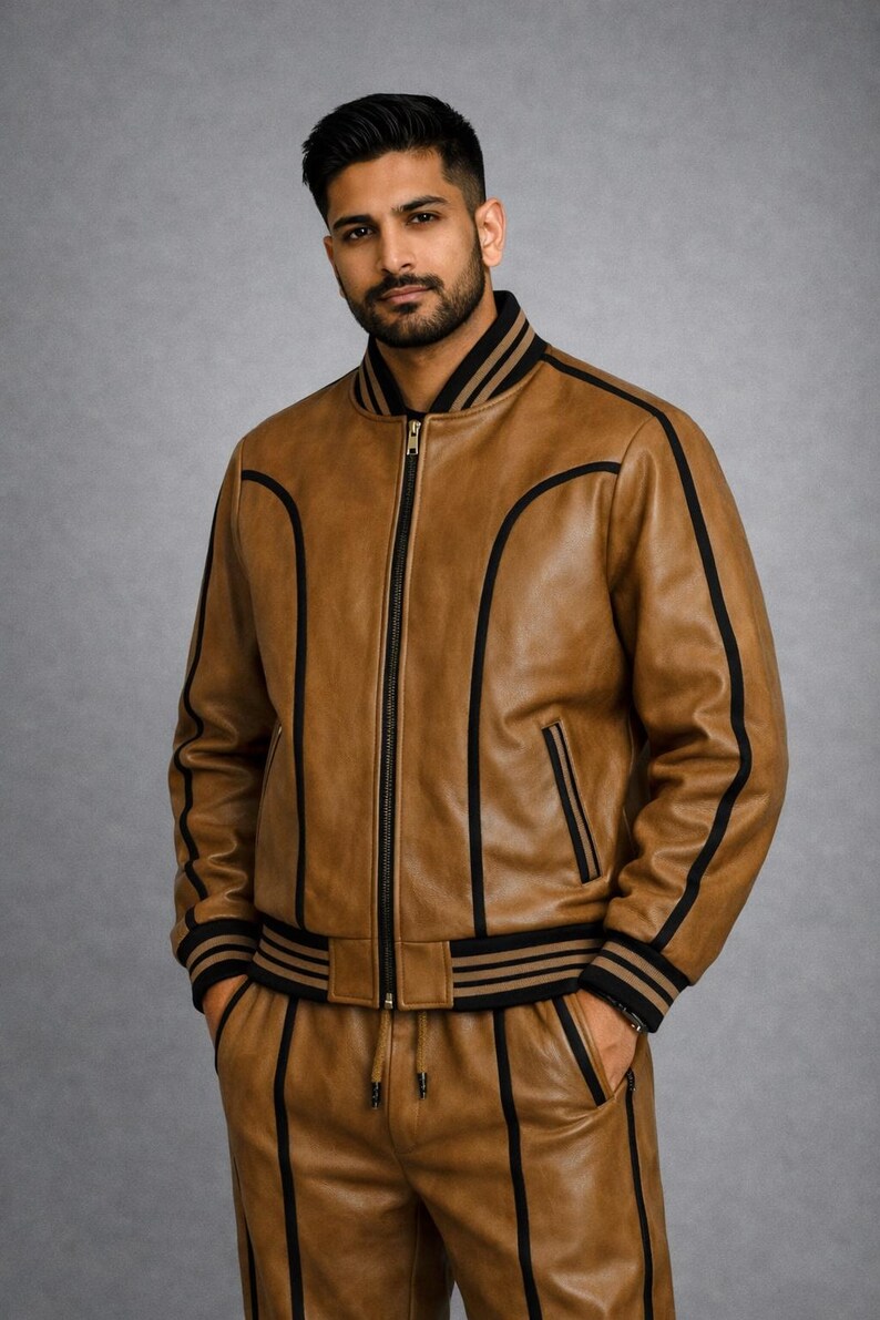 Pu&ograve; includere: Giacca bomber e pantaloni coordinati in pelle marrone con strisce e finiture nere. La giacca ha una chiusura con zip frontale e colletto e polsini a coste. I pantaloni hanno una vita con coulisse e tasche.