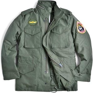 Puede incluir: Chaqueta verde oliva de estilo militar con cremallera, múltiples bolsillos y cuello alzado. Presenta un parche con un emblema alado en el pecho y un parche de "Yong Company" en la manga. La chaqueta tiene un cordón en la cintura.