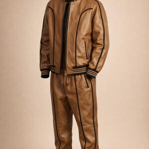 Pu&ograve; includere: Una tuta in pelle marrone chiaro composta da un bomber e pantaloni abbinati. La giacca ha strisce nere e un colletto nero. I pantaloni hanno una vita con coulisse e strisce nere sui lati. L'outfit &egrave; in pelle.