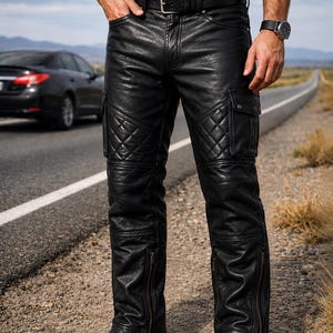 May include: Black leather pants featuring a quilted diamond pattern on the thighs, side cargo pockets with snap closures, and vertical zippered openings at the lower legs. The pants include a black leather belt with a silver-toned metal buckle.
