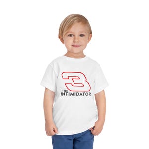 May include: A white toddler t-shirt featuring a red outlined number 3 and the text "THE INTIMIDATOR" in black. The shirt is worn by a young child, and the design is centered on the front.