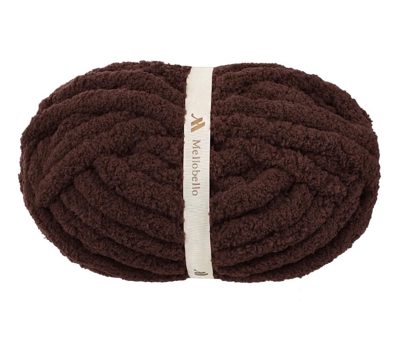May include: A skein of dark brown, thick, plush yarn wrapped in a cream-colored paper band. The band features the text Mellobello printed in a dark brown font, along with a small logo icon above the brand name and another below it.
