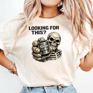 Puede incluir: Camiseta color crema con el texto "LOOKING FOR THIS?" sobre un gráfico de un esqueleto sosteniendo una llave de vaso de 10 mm. La mano del esqueleto y la llave están representadas con detalle.
