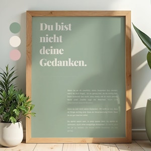 Könnte beinhalten: Ein gerahmter Druck mit dem deutschen Text "Du bist nicht deine Gedanken" in Weiß auf hellgrünem Hintergrund. Der Holzrahmen umgibt den Druck. Eine kleine Pflanze ist links zu sehen.