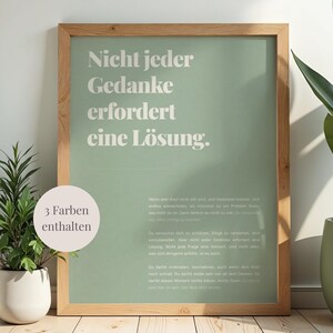 May include: A framed poster with the text "Nicht jeder Gedanke erfordert eine Lösung" in a light green font on a sage green background. The frame is made of light brown wood. A small plant in a white pot is visible.