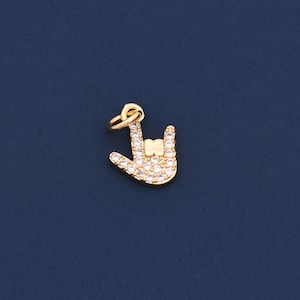 May include: A gold-coloured charm in the shape of a hand making the "I love you" sign. The charm is encrusted with small, clear crystals. The background is a solid, dark blue colour. This charm is suitable for jewellery making.