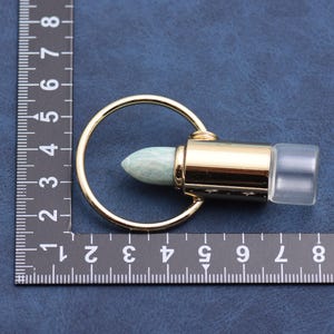 May include: A gold-colored metal essential oil bottle roller with a light green stone rollerball and a clear plastic cap. The rollerball is attached to a gold-colored metal cylinder and a gold-colored metal ring.