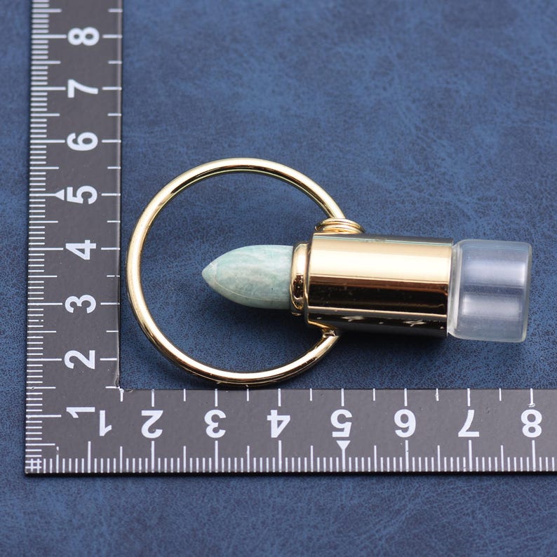 May include: A gold-colored metal essential oil bottle roller with a light green stone rollerball and a clear plastic cap. The rollerball is attached to a gold-colored metal cylinder and a gold-colored metal ring.
