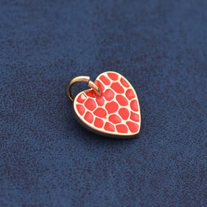 May include: A heart-shaped pendant with a gold-colored border and bail. The heart is filled with a red pattern, and the background is a dark blue. This jewelry item is suitable for necklaces or bracelets.