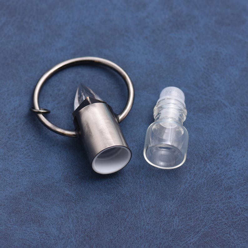 May include: A silver-colored wine bottle stopper with a clear, pointed crystal and a ring handle. Beside it is a small, clear glass bottle with a rollerball top. The items are on a blue surface.