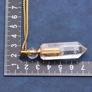 Puede incluir: Un collar con colgante de cristal de cuarzo transparente con una cadena dorada. El colgante es un cristal transparente y alargado con un tubo de metal dorado en su interior. El collar mide unos 7.6 cm de largo.