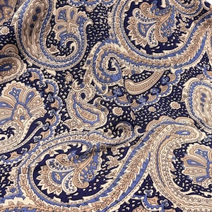 Puede incluir: Una tela con un denso estampado de cachemira en tonos azul marino profundo, bronceado claro y azul bígaro. El intrincado diseño consiste en formas de lágrima arremolinadas, motivos florales y líneas finas, creando un estampado textil continuo y repetitivo.