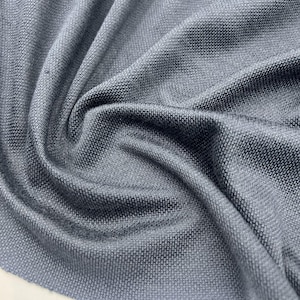 May include: Close-up of a textured, gray fabric with a subtle sheen. The material is tightly woven, creating a pattern of small, raised squares. The fabric is draped, showing folds and shadows that highlight its texture and depth.