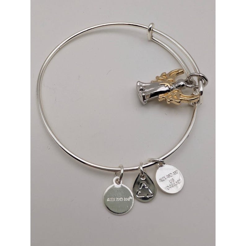 Pode incluir: Uma pulseira de fio expans&iacute;vel em tom prateado com um pingente de anjo bicolor com asas em tom dourado. Tr&ecirc;s pequenos pingentes circulares e em forma de gota pendem do fio, cada um gravado com a marca Alex and Ani e um s&iacute;mbolo de reciclagem.