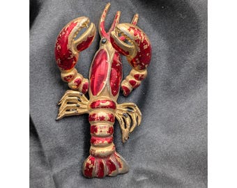 Broche vintage em formato de lagosta, nas cores vermelho e dourado, com 7,6 cm de comprimento, em metal esmaltado com mecanismo de tremor. Estilo náutico.