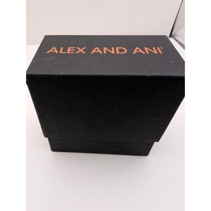 Pode incluir: Uma caixa de joias retangular preta com tampa. O topo da tampa apresenta o texto ALEX AND ANI impresso em uma cor cobre met&aacute;lica. A caixa tem um acabamento fosco e um design estruturado, consistindo em uma base e uma tampa remov&iacute;vel.