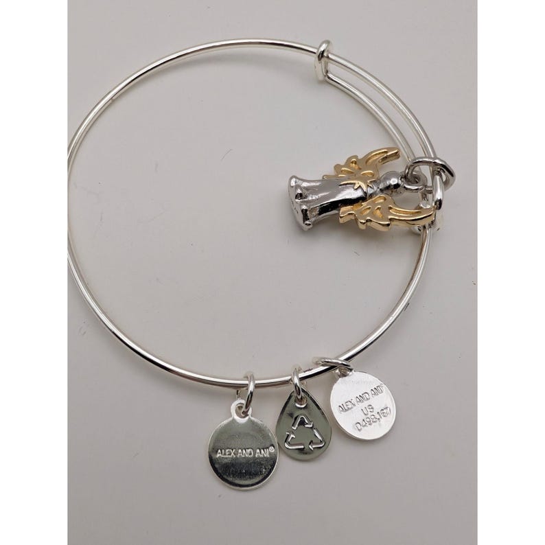 Pode incluir: Uma pulseira de fio expans&iacute;vel em tom prateado com um pingente de anjo bicolor com asas em tom dourado. Tr&ecirc;s pingentes adicionais em formato circular e de gota em tom prateado est&atilde;o fixados, cada um gravado com a marca Alex and Ani.