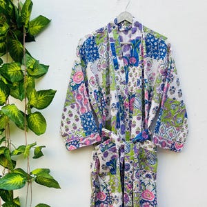 May include: A colorful, patterned robe with a floral design. The robe features a patchwork of blue, pink, green, and purple floral patterns on a white background. It has long sleeves and a matching belt.