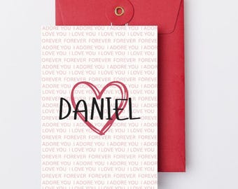 May include: A red greeting card and envelope set. The card features the name "DANIEL" inside a red heart, with the words "I ADORE YOU" and "FOREVER" printed repeatedly in a light pink font.