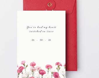 May include: A greeting card with the text "You've had my heart switched on since" and the date "24. 02. 24". The card features a floral border of pink and white carnations and is paired with a red envelope.