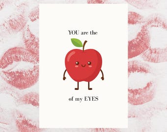 May include: A white greeting card with the text "YOU are the of my EYES" and a cartoon red apple with a green leaf. The background features a pattern of red lipstick kiss marks.