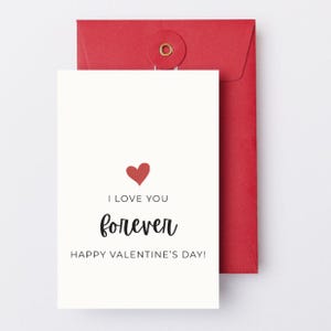 May include: A white Valentine's Day card with a red heart and the words "I LOVE YOU forever HAPPY VALENTINE'S DAY!" is placed in front of a red envelope.