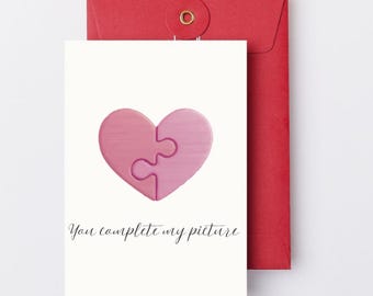 May include: A greeting card with a pink heart puzzle design and the text "You complete my picture." The card is paired with a red envelope.
