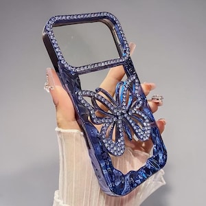 Könnte beinhalten: Blaue Handyhülle mit Schmetterlingsdesign. Die Hülle ist mit glitzernden Strasssteinen an den Rändern und auf dem Schmetterling verziert. Die Hülle hat eine glänzende Oberfläche und eine transparente Öffnung für die Kamera.