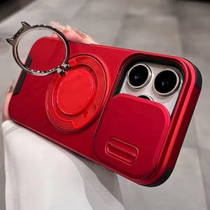 Puede incluir: Funda de teléfono roja con tapa de lente de cámara integrada y soporte de anillo. La funda tiene un acabado brillante y un borde negro. El soporte del anillo es plateado y tiene un diseño circular.