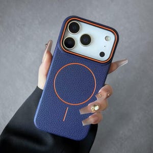 Könnte beinhalten: Marineblaue Handyhülle mit orangefarbenem Rand und passendem orangefarbenem Kreisdesign. Die Hülle hat eine strukturierte Oberfläche und ein weißes Kameramodul mit drei Objektiven.