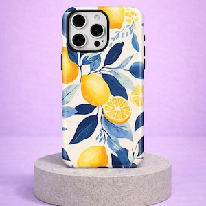 Könnte beinhalten: Eine Handyhülle mit einem lebendigen Zitronen- und Blättermuster. Die Hülle hat einen weißen Hintergrund mit gelben Zitronen, blauen Blättern und kleinen gelben Blüten. Sie wird auf einem grauen Steinsockel vor einem lila Hintergrund präsentiert.