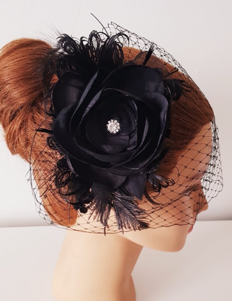 May include: Black bridal hair comb with a large black satin flower, black feathers, and a black birdcage veil.