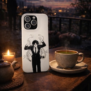 May include: White phone case featuring a black and white illustration of a person in a suit with a fish design. The case is on a wooden table next to a lit candle, a cup of tea, and a small teapot. The background shows a city skyline at dusk.