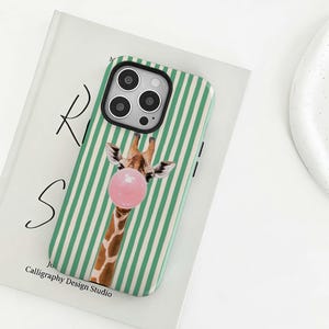 May include: A phone case with a green and white striped pattern. The case features a giraffe blowing a pink bubblegum bubble. The text "Calligraphy Design Studio" is printed at the bottom of the case.