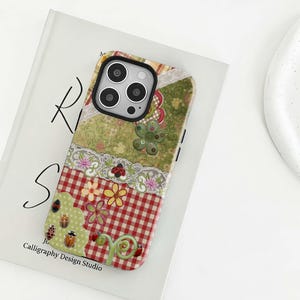 Peut inclure: Coque de téléphone décorative avec un motif patchwork. Le boîtier présente un motif à carreaux rouges et blancs, des motifs floraux et d'insectes, et une bordure en dentelle. Le texte "Calligraphy Design Studio" est visible.