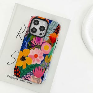 Könnte beinhalten: Eine farbenfrohe Handyhülle mit floralem Design. Die Hülle zeigt eine Mischung aus gelben, rosa, orangefarbenen und blauen Blumen und Blättern. Der Text "Calligraphy Design Studio" ist unten links sichtbar.