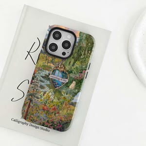 Könnte beinhalten: Eine Smartphone-Hülle mit einer lebendigen, detaillierten Landschaftsillustration eines üppigen Gartens mit Blumen, Bäumen, einem kleinen Reh und einer Katze. Ein goldfarbenes herzförmiges Emblem ist mittig mit dem Text everything, in time.