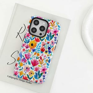 May include: A floral phone case featuring a vibrant watercolor design. The case showcases a white background adorned with colorful flowers in shades of pink, yellow, blue, and red. The text "Calligraphy Design Studio" is visible on the case.