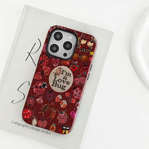 Könnte beinhalten: Eine weinrote Handyhülle mit einem Marienkäfermuster. Die Hülle zeigt verschiedene Marienkäfer-Illustrationen und den Text "I'm a Love Bug". Die Hülle liegt auf einer weißen Oberfläche mit dem Text "Calligraphy Design Studio."