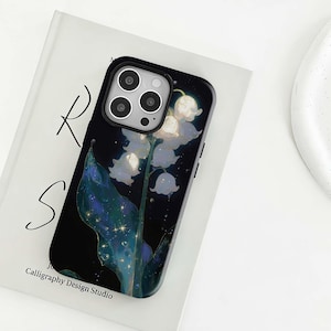 Könnte beinhalten: Schwarze Handyhülle mit floralem Design aus weißen Maiglöckchenblüten, grünen Blättern und sternenklarem Hintergrund. Die Hülle liegt auf einem weißen Buch mit dem Text "R S" und "Calligraphy Design Studio".