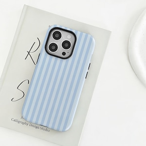 May include: A light blue and white vertically striped smartphone case with a black camera module housing three circular lenses and a flash, designed to fit a device with a square-shaped camera cutout on the upper left corner.