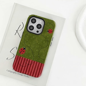 May include: Green phone case with a ladybug design. The case features a green background with a pattern of white stars and dotted lines. Two red ladybugs are visible. The bottom of the case has a red and white striped pattern. The text "Calligraphy Design Studio" is printed on the bottom.