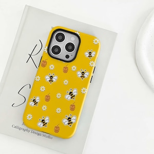 Könnte beinhalten: Gelbe Handyhülle mit einem Bienen- und Gänseblümchenmuster. Die Hülle hat einen schwarzen Kamerarahmen und den Text "Calligraphy Design Studio". Das Design umfasst Cartoon-Bienen, Gänseblümchen und Honigtöpfe.