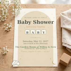 Pode incluir: Um convite retangular para chá de bebê com um design de arco bege, o texto "Please join us for a Baby Shower honoring Sophia", a palavra "BABY" em peças de letras e os detalhes do evento para sábado, 22 de maio de 2027.