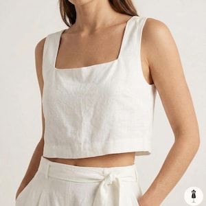 Puede incluir: Un top corto de lino blanco con cuello cuadrado. El top sin mangas se combina con pantalones de cintura alta a juego. El conjunto está hecho de una tela ligera y texturizada. El top tiene un diseño limpio y minimalista.