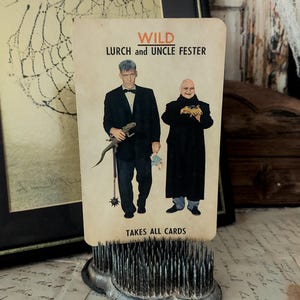 May include: A playing card with a white background and black text. The card is titled "WILD LURCH and UNCLE FESTER" and says "TAKES ALL CARDS". The card features a photo of Lurch and Uncle Fester from the Addams Family.