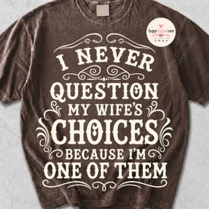 Puede incluir: Una camiseta de manga corta de color marrón oscuro con texto blanco que dice I NEVER QUESTION MY WIFE'S CHOICES BECAUSE I'M ONE OF THEM. El diseño incluye adornos decorativos y un logotipo circular en la esquina superior derecha con el texto happy digipodzone.