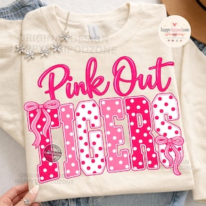 May include: A cream-colored long-sleeve sweatshirt featuring the text Pink Out in bright pink script above the word TIGERS in large block letters. The letters are filled with a pink and white polka dot pattern and accented with pink bows.