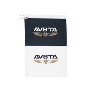 Op de afbeelding: Een marineblauwe en witte golfhanddoek met de gouden tekst "AV8TA" en een propeller- en vleugelontwerp. De handdoek heeft een messing oogje om op te hangen. Ongeveer 30 cm lang.